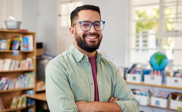 A man in a library wearing a green shirt and glasses with his arms crossed.