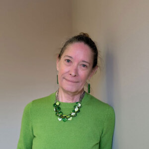 Woman with with her hair in a bun wearing a bright green sweater and green and white necklace