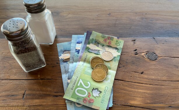 A stack of Canadian bills and change on a table beside a salt and pepper shaker