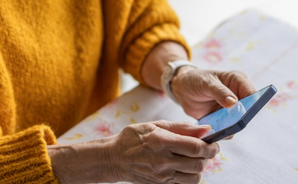 The arms of an older woman in an orange sweater holding a cell phone