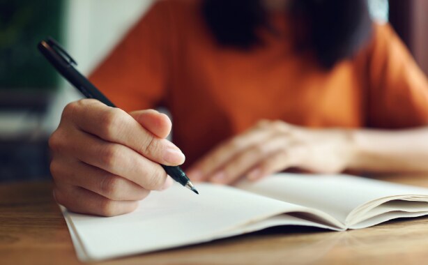 A woman's hands writing in an open note book